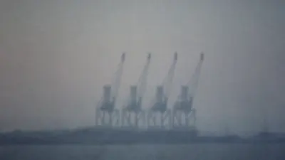 Sagome di gru portuali all'orizzonte nella foschia dell'alba sul mare